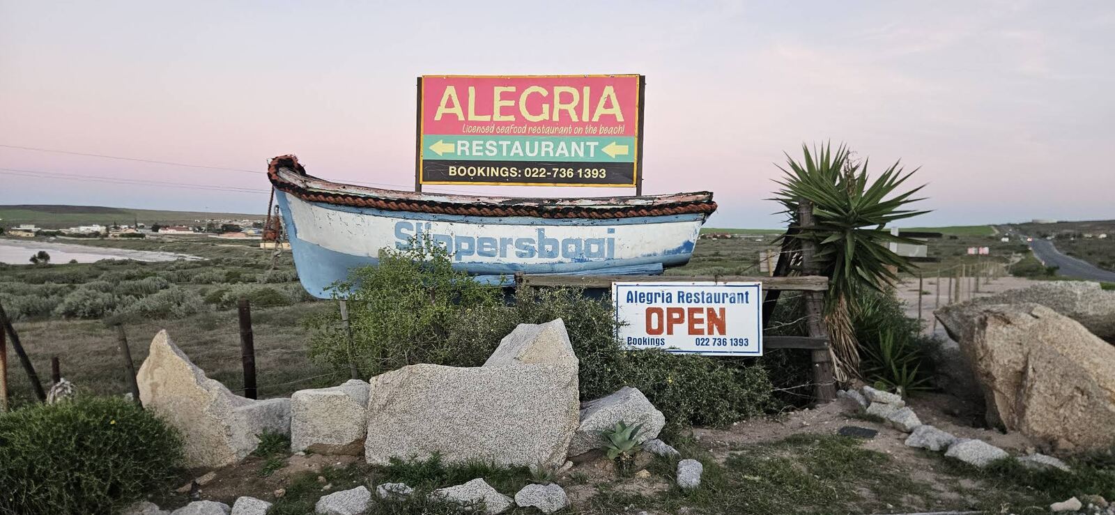 The Alegria roadside sign and the Slippersbaai boat at sunset